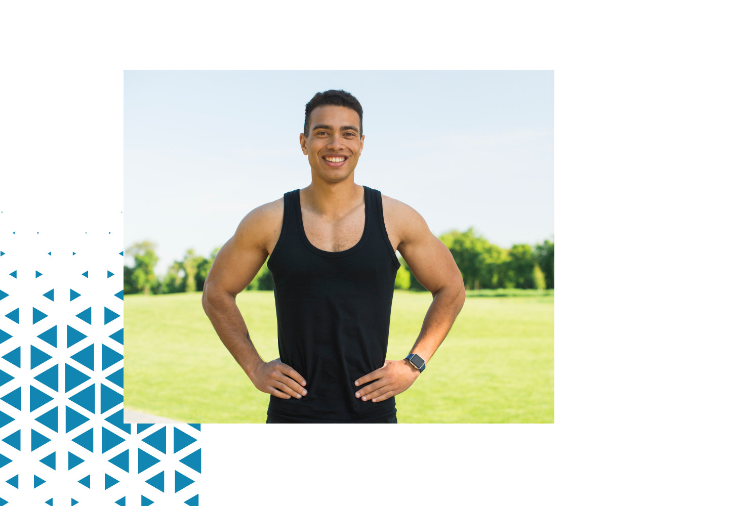 A man standing outdoors in a park, smiling, wearing a black tank top and smartwatch, with hands on his hips