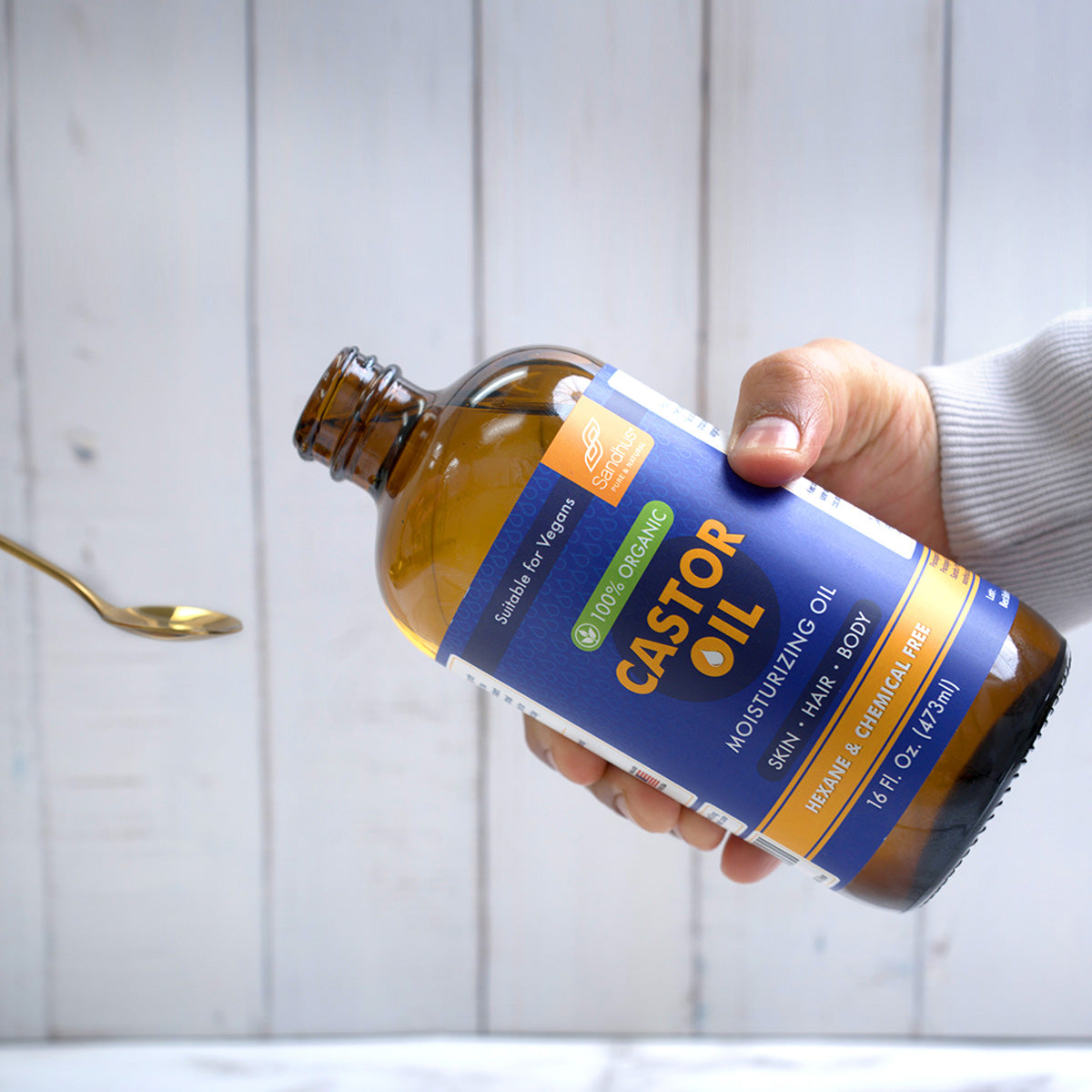 Hand holding a bottle of castor oil with a label against a white wooden background