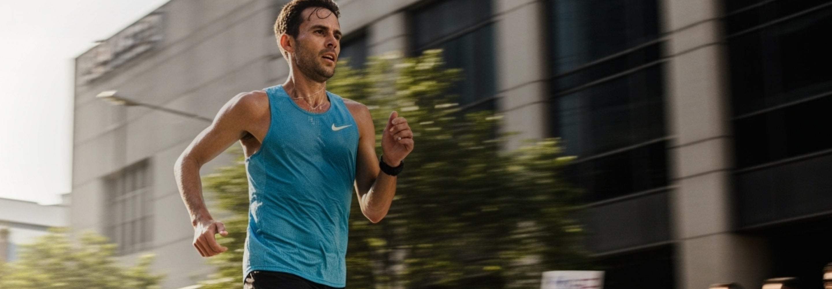 Man running on a city street wearing a blue Nike tank top.
