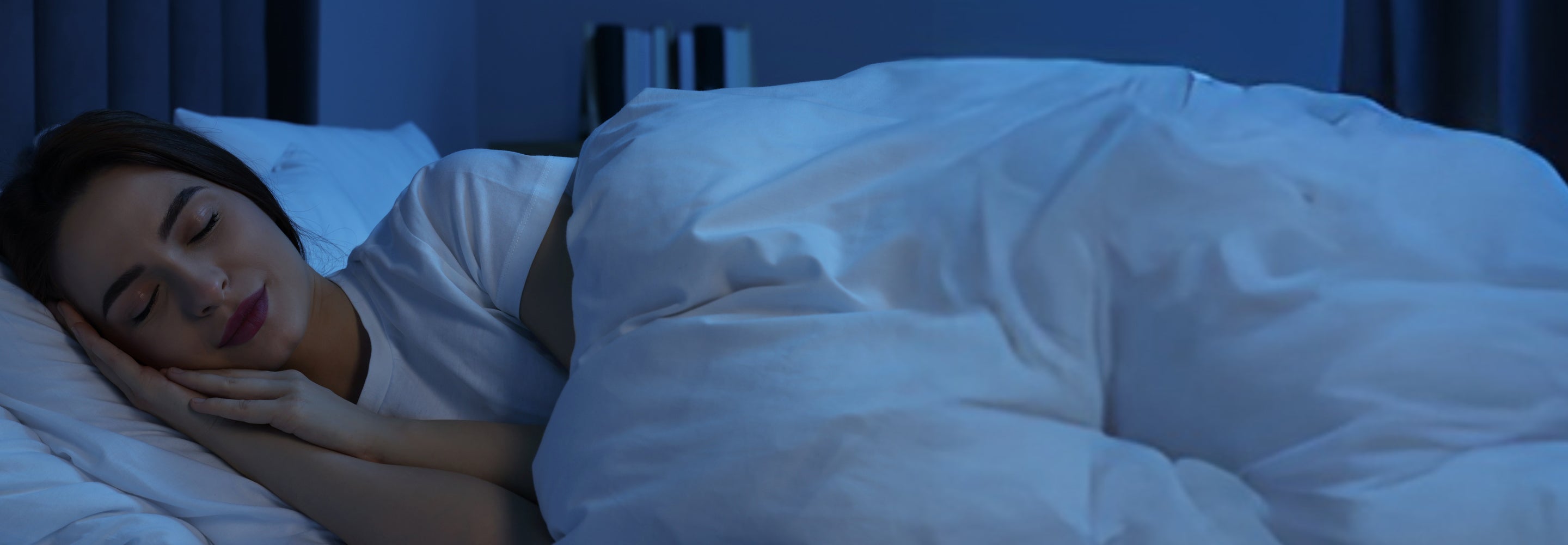 Woman sleeping peacefully under a white duvet in a dimly lit bedroom.