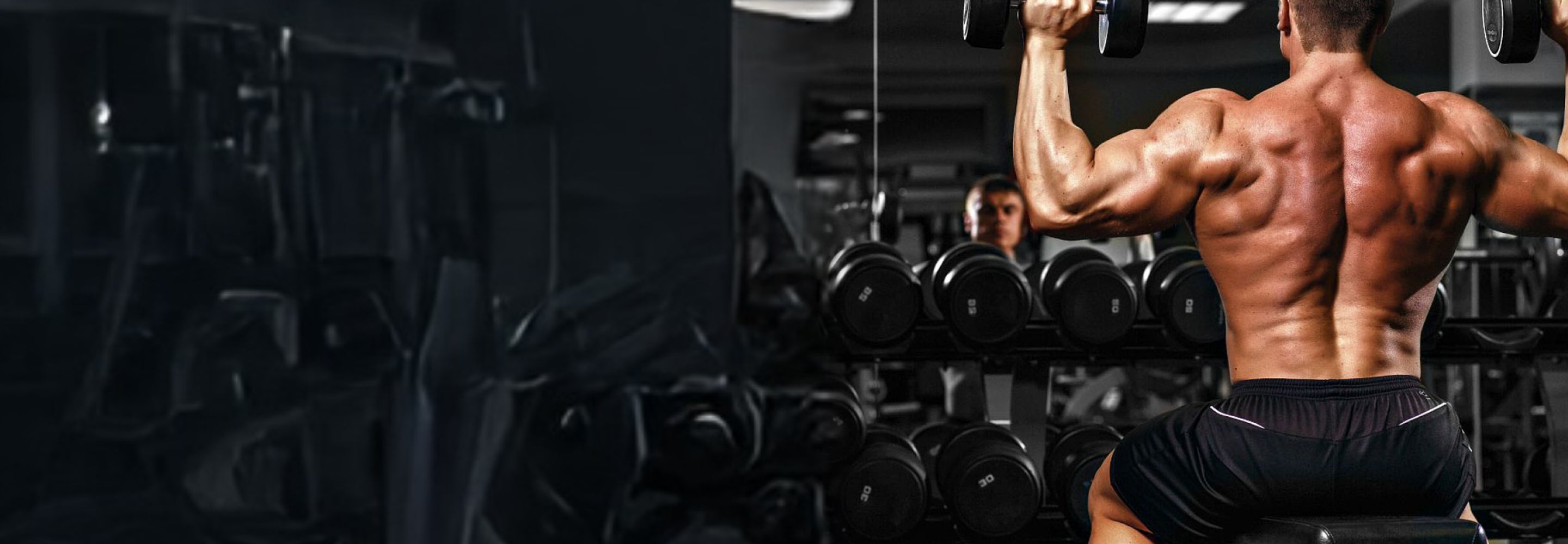 Muscular man flexing his arm in a gym setting with weights and mirrors.
