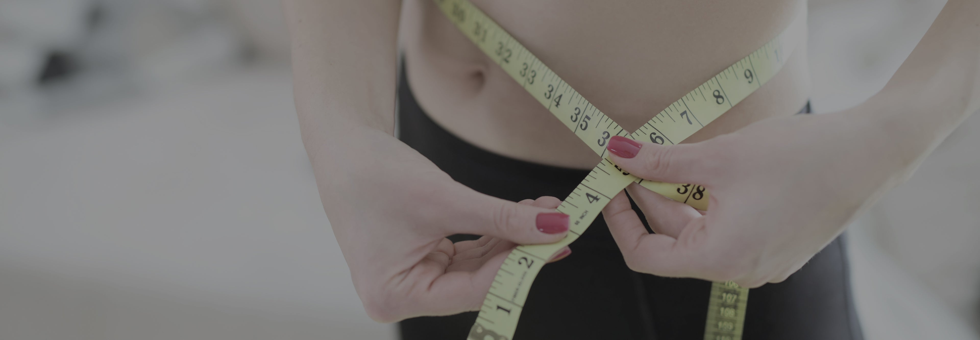 Person measuring waist with a tape measure on a blurred background