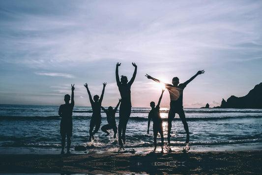 Group of friends jumping and celebrating at the beach during sunset, symbolizing energy and well-being while traveling.