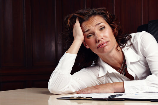 Exhausted middle-aged woman leaning on desk with paperwork, showing stress, brain fog, and menopause-related fatigue symptoms