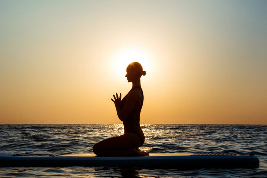 Woman practicing calming yoga on a paddleboard during sunset, illustrating relaxation, focus, and magnesium’s role in mental clarity.
