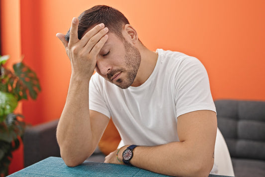 Man sitting tired and holding his head, illustrating fatigue and low energy that may be linked to poor liver health and toxin buildup.