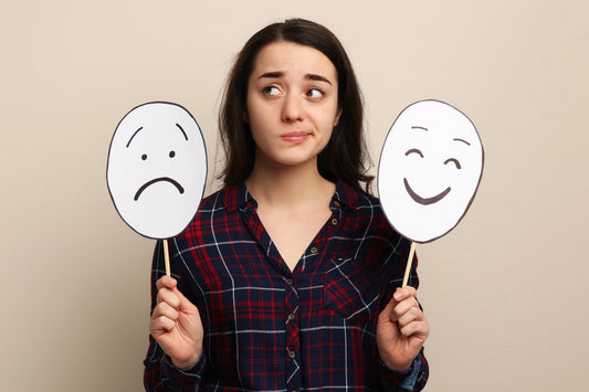 Woman holding happy and sad emotion masks representing PMS mood swings and emotional fluctuations