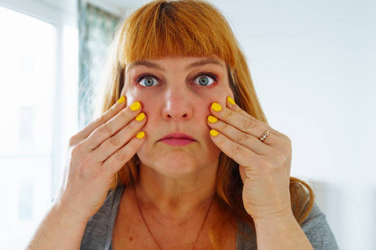Woman touching her cheeks while looking in the mirror, showing facial puffiness commonly experienced during menopause.