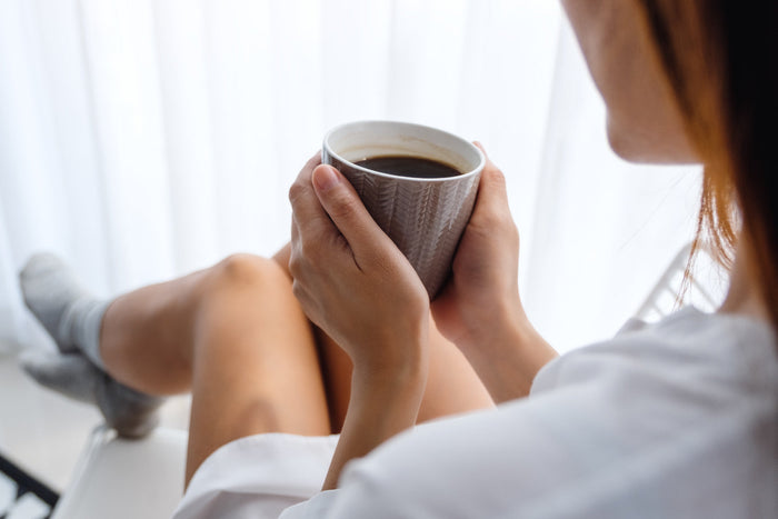 Woman relaxing with a cup of black coffee, illustrating mindful morning coffee consumption for metabolic health.