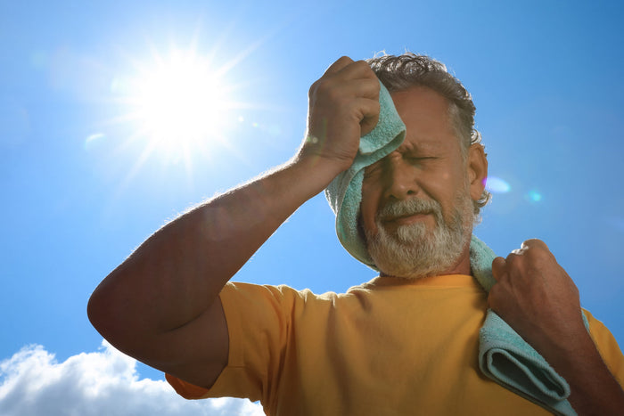 Man wiping sweat under the bright summer sun, illustrating how heat, dehydration and lifestyle factors may contribute to summer fatigue.