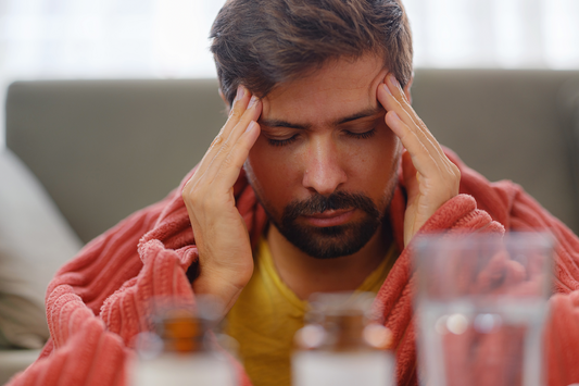 Man sitting with eyes closed holding his head in stress, showing fatigue and mental strain affecting immunity.