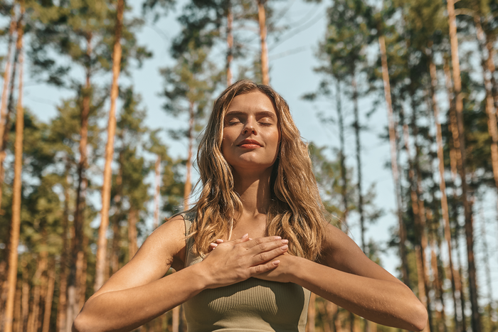 Woman in a forest with hands on chest practicing calm breathing to illustrate natural lung wellness support