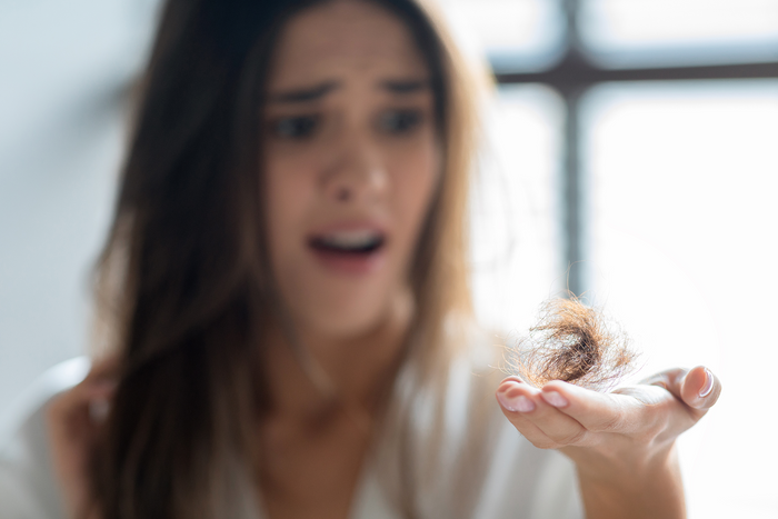 Concerned woman holding fallen hair in hand showing sudden hair shedding, thinning concerns and early hair loss signs