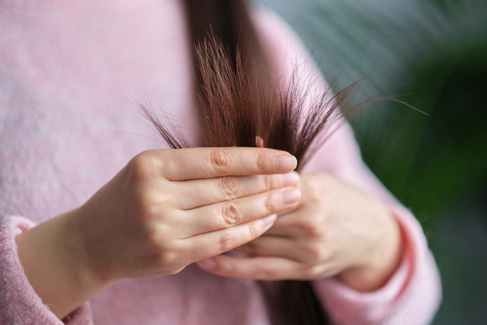 Close-up of a woman holding broken hair strands, illustrating hair breakage, thinning hair concerns, and the need for targeted hair support.