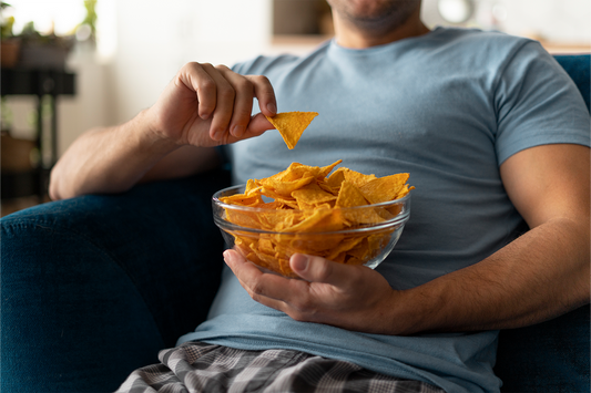 Person constantly snacking on chips while relaxing at home, illustrating how frequent snacking may influence everyday dietary habits and liver health.