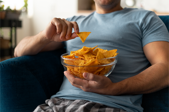 Person constantly snacking on chips while relaxing at home, illustrating how frequent snacking may influence everyday dietary habits and liver health.