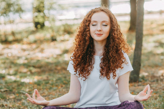 Woman sitting outdoors in a peaceful meditation pose with eyes closed, promoting calmness and mental clarity.
