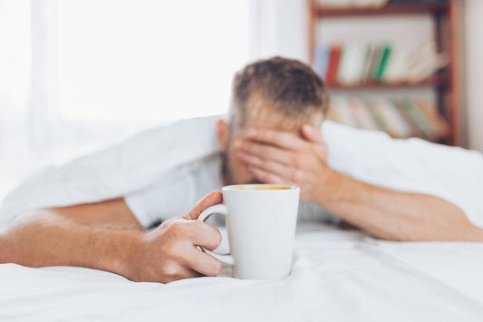 Tired man in bed holding a coffee cup showing morning grogginess, fatigue, and low energy after sleep