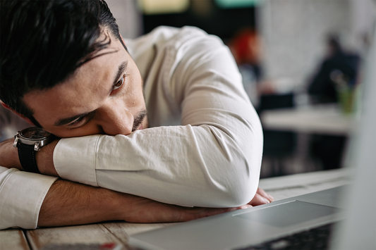 Man resting with his head on folded arms beside a laptop, illustrating mental fatigue and the drained feeling that can follow prolonged cognitive work.