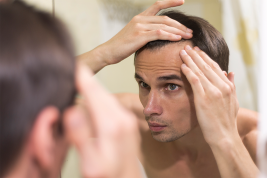 A man examines his hairline in a mirror, gently lifting his hair to assess changes in hair density and the appearance of more fuller hair.
