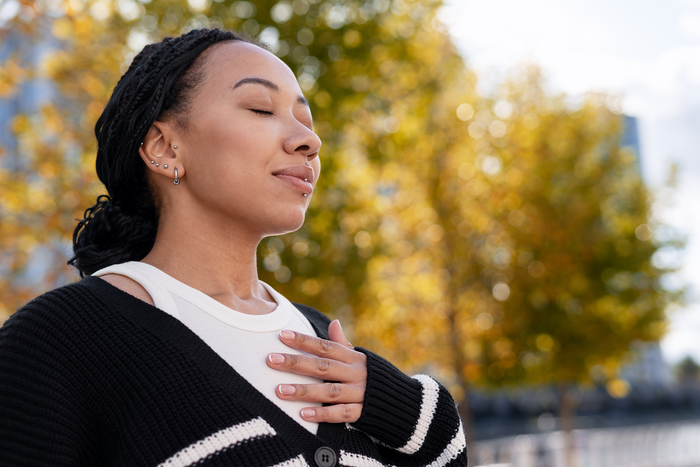 Woman practicing deep breathing with hand on chest outdoors, symbolizing improved lung function and natural breathing support