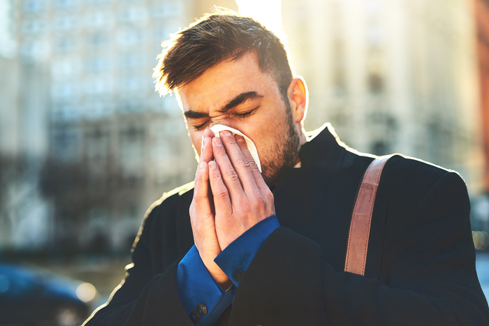 Man sneezing into tissue outdoors during pollen season representing seasonal allergies causing congestion and mental fog.