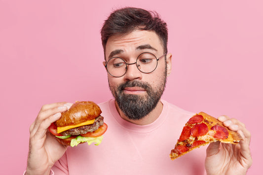 Man choosing between burger and pizza, illustrating strong afternoon junk food cravings and unhealthy snack temptations.