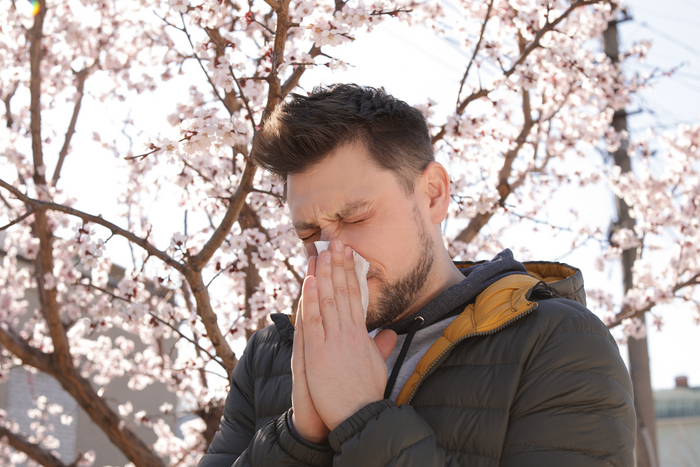 Man sneezing outdoors during spring allergy season showing immune stress and seasonal sensitivity from pollen exposure