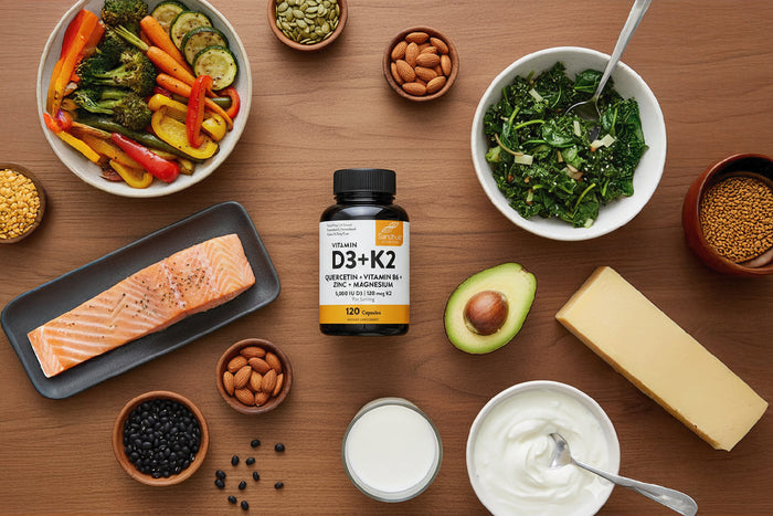 Vitamin D3 + K2 supplement bottle with salmon, avocado, nuts, and greens for bone and heart health.