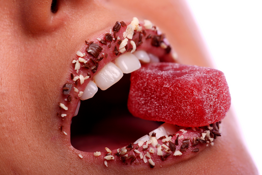 Close-up of a person biting a red sugar-coated gummy candy, illustrating sweet cravings and the desire for sugary foods associated with a sweet tooth.