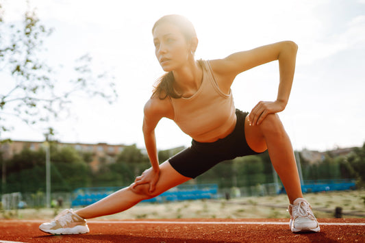 Athletic woman stretching her legs on a running track in sunlight, highlighting the importance of flexibility, movement, and nutrients that support strong bones