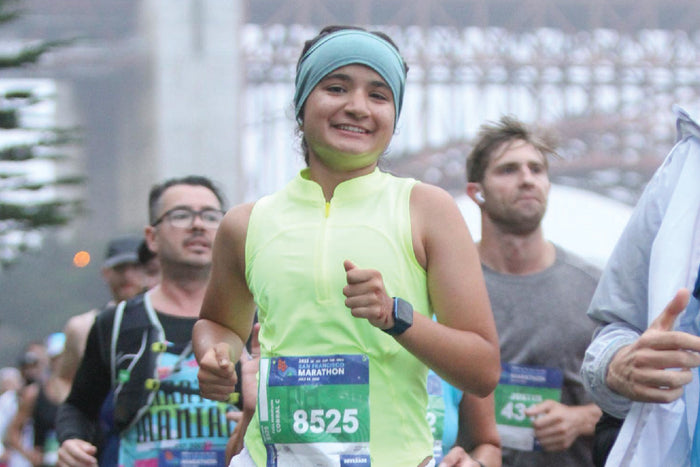 Anna Sandhu, 13-year-old runner, completing the San Francisco Marathon with a smile, wearing a neon yellow top and headband.