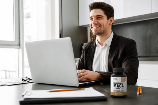 Smiling man works on a laptop beside Sandhus Ashwagandha Maca Fenugreek capsules, illustrating maca energy support for busy daily work.
