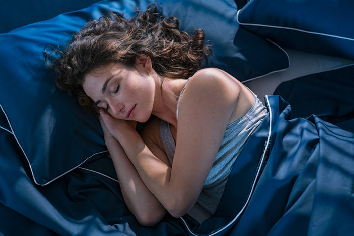 Woman sleeping peacefully on blue bedding during the night, illustrating healthy sleep cycles, deep sleep, REM sleep, and better sleep quality.