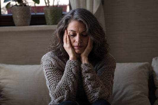 Middle-aged woman sitting on a sofa with her hands on her face, representing stress, emotional changes, and mood shifts during menopause.