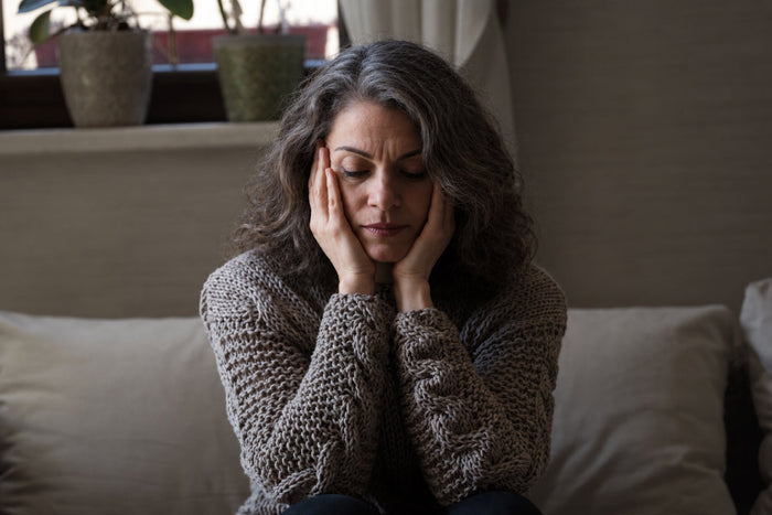 Middle-aged woman sitting on a sofa with her hands on her face, representing stress, emotional changes, and mood shifts during menopause.