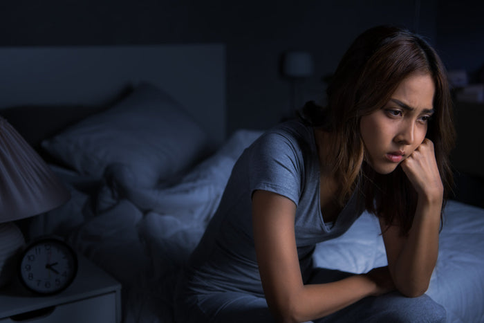 Woman sitting awake in bed at night with racing thoughts and difficulty relaxing before sleep