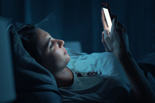 Person lying in bed at night while looking at a smartphone, highlighting the 10 PM scrolling habit before sleep.