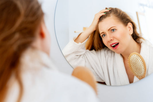 Woman examining hair in a mirror with a hairbrush, illustrating seasonal hair shedding, changes in hair follicles, and maintaining healthy hair year-round.