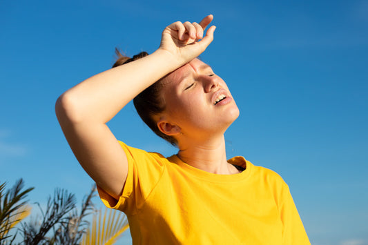 Person shielding face from bright sun on a hot day, illustrating summer fatigue, dehydration, heat stress, and low energy.