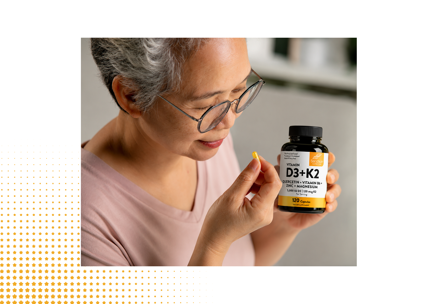 An older woman with gray hair and glasses holds a small yellow supplement capsule in her hand while looking at a black bottle labeled D3+K2. The photo is cropped and presented within a white layout that includes a yellow dot pattern on the bottom left.