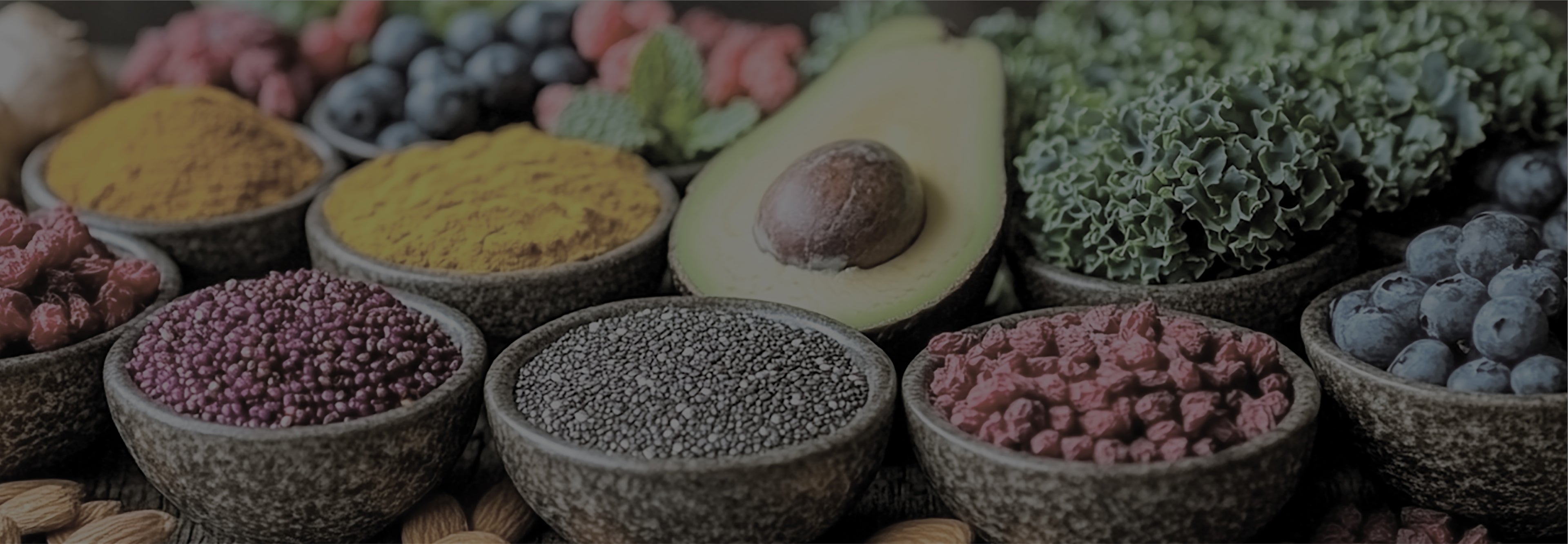 Assorted spices and herbs with an avocado in the center on a dark background