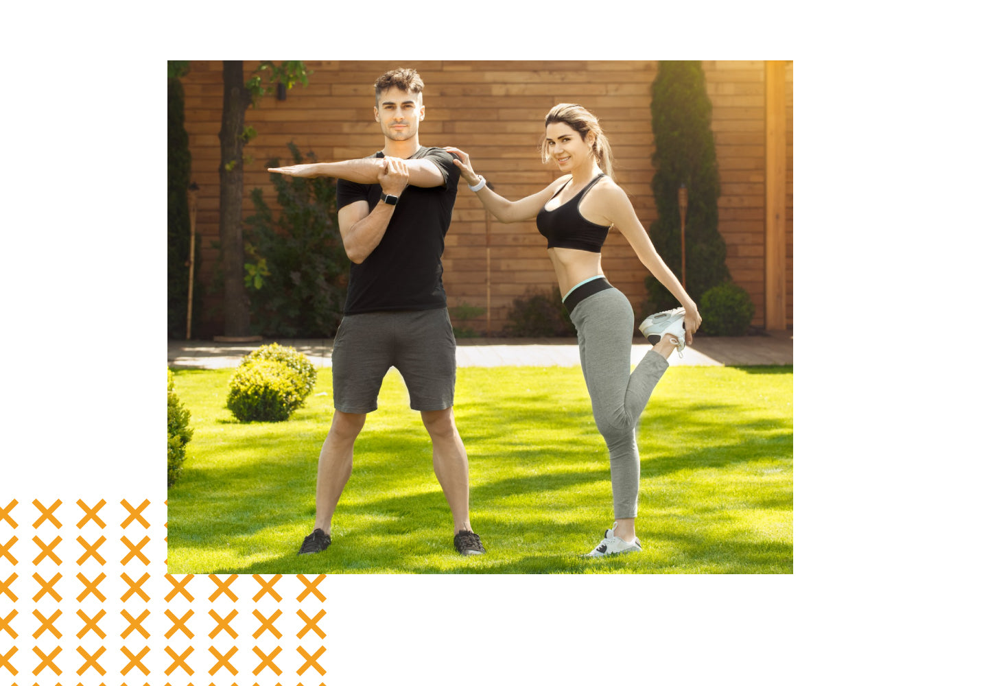 Two people exercising outdoors on a grassy area with a wooden fence and plants in the background.