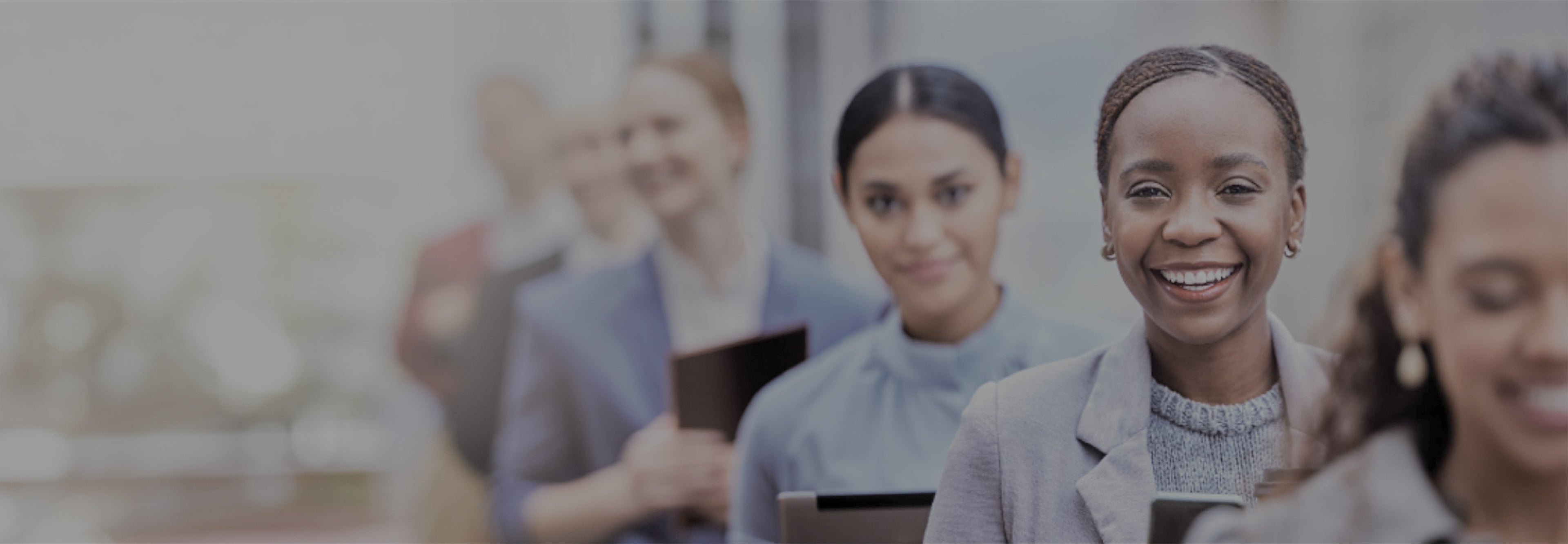 Group of people in a blurred office setting with a focus on a woman smiling.