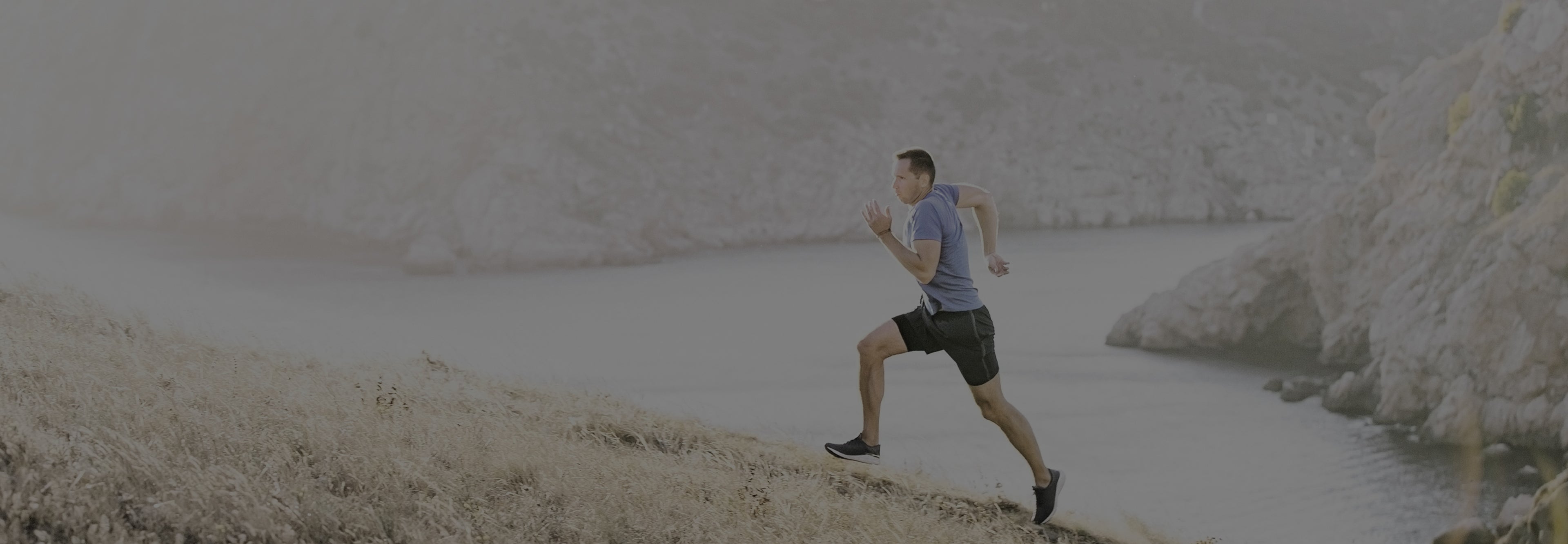 Person running along a rocky path by a body of water